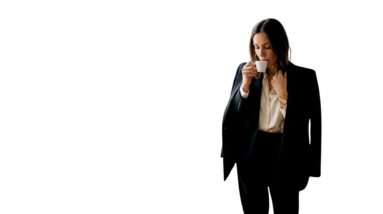 Une femme ajuste son blazer près d’une fenêtre, entourée de magazines de mode.