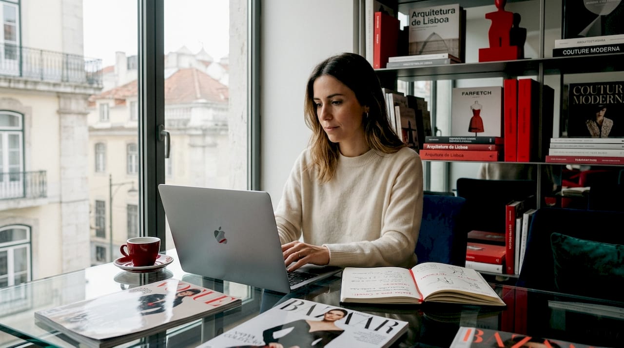 Sentada confortavelmente à mesa de casa, uma mulher faz compras de moda de luxo online.