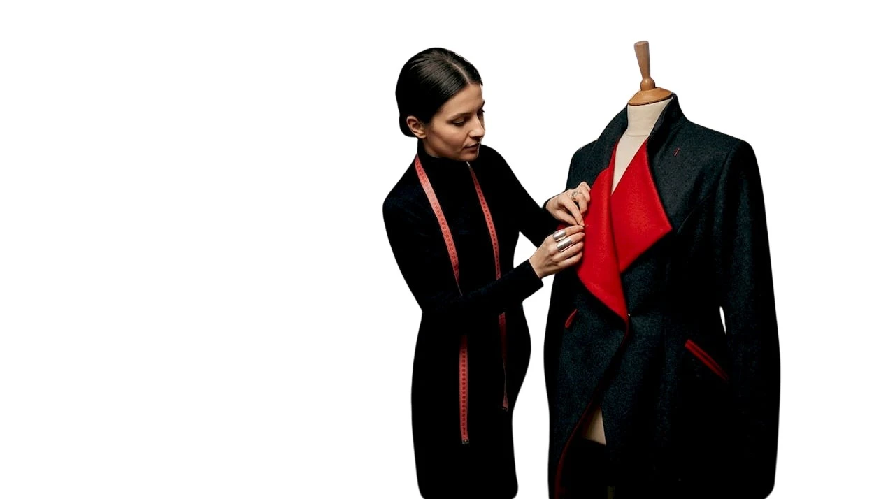 Creatoare de modă la lucru în atelier, concentrată pe schițe și materialele din jur.